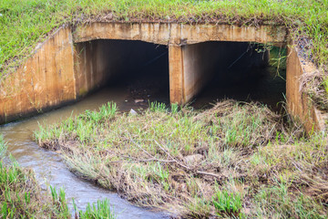 Reinforced concrete box culverts under the asphalt road. Box culvert is a structure that allows water to flow under a road, railroad, trail, or similar obstruction from one side to the other side. - obrazy, fototapety, plakaty