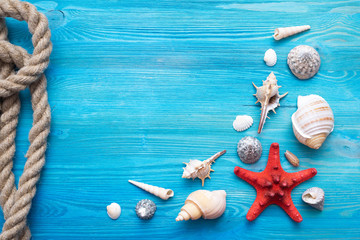 Summer sea vacation concept background with copy space. Various seashells, mooring rope and a red starfish on a blue wooden floor background.