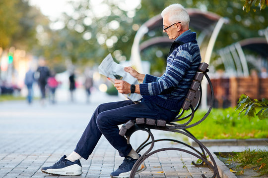 Old grey-haired man sit on the bench and reading a newspaper