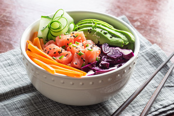 Hawaiian Poke Bowl with Sliced Salmon, Avocado, Cucumber, Purple Cabbage, and Carrots over Brown Rice with Chopsticks