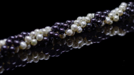 Two mixed strands of natural black pearl beads on a black background with reflection
