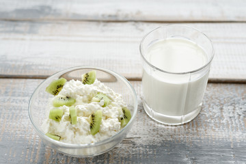 Frontally on grey wooden background cottage cheese in bowl with kiwi fruit, soft light, healthy food concept.