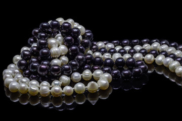 Two mixed strands of natural black pearl beads on a black background with reflection