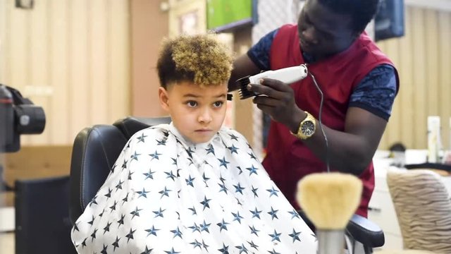 Boy in the african barbershop. Cute mixed boy makes a haircut in the African salon. Hair style. Haircut by machine for children. School boy hair style. Haircut 