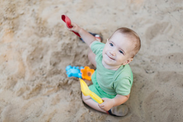 Fototapeta premium Little child in sandpit. Portrait of happy little baby boy enjoying playing with sand toys on summer day.