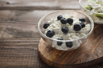 Close-up of bowl of cottage cheese and blueberries on natural wooden stand in the natural light