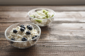close-up of homemade cottage cheese with blueberries and kiwis in glass bowls on a wooden background. Selective focus.