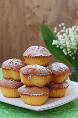 Cupcakes with semolina on kefir on a white plate.Nearby is a jug with lilies of the valley
