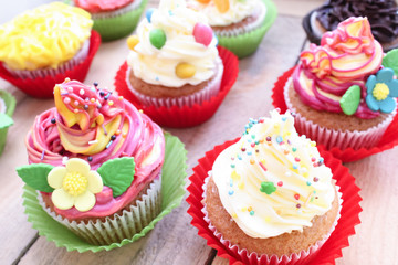 Colorful cupcakes with vanilla cream, sugar flowers and chocolate covered peanuts. Сlose-up