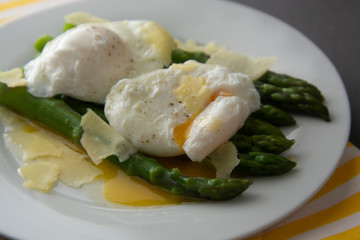 Close up asparagus salad with poached egg and parmesan cheese. Gray background. Healthy, tasty breakfast.