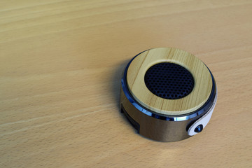 Small round shape wireless speaker with wooden top on wooden table.