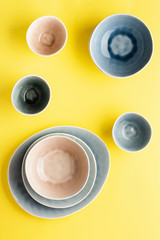 Obraz na płótnie Canvas Beautiful blue, grey, beige dinnerware, plates bowls on yellow background table, top view, selective focus