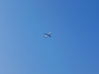 An airplane flying across blue sky, from a far distance, in a sunny day in summer time