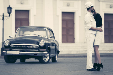Happy young fashion couple in love embracing next to vintage car