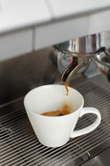 Close-up of freshly brewed coffee is poured from a coffee machine into a white cup