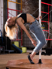 Young woman in ripped jeans performing pole dance