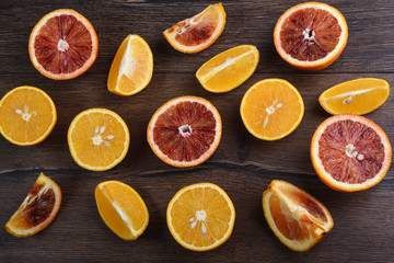 Ripe juicy slices of blood and ordinary oranges on a wooden background.