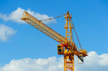 Yellow construction tower crane, heavy industry, blue sky and white clouds on background