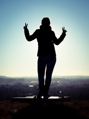 Image of woman's silhouette performing victory sign with fingers standing on a platform