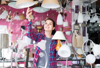 girl in lighter shop choosing  modern glass chandelier for house interior