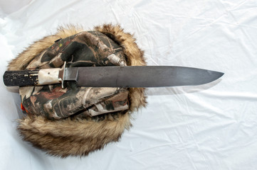 A big mountain man bowie knife displayed on a warm furry hat with a white background.