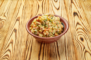 Russian traditional Christmas and New year salad Olivier with vegetables and meat on a plate with wooden background