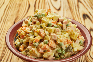 Russian traditional Christmas and New year salad Olivier with vegetables and meat on a plate with wooden background