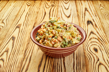 Russian traditional Christmas and New year salad Olivier with vegetables and meat on a plate with wooden background