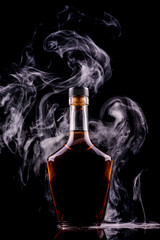 bottle and glass of whiskey or cognac with smoke on dark background