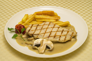 Chicken steak.  Chicken steak with roasted potatoes and mushroom sauce. Chicken steak is served with a piece of mushroom and red roasted pepper for decoration. Place on a white ceramic plate.