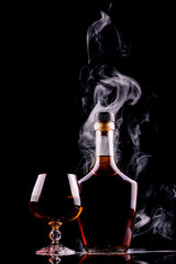 bottle and glass of whiskey or cognac with smoke on dark background