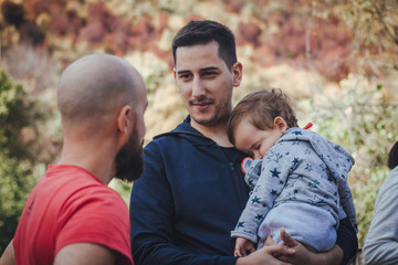 Two men talking and one of them holding a child