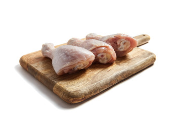 Chicken legs with skin lying on a wooden cutting board. Poultry meat isolated on white background