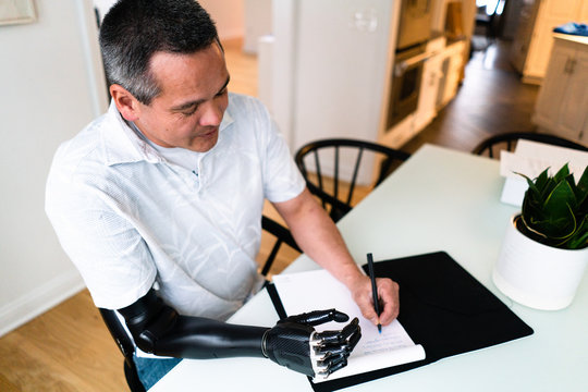 Man rests his robotic arm on table and writes in ledger