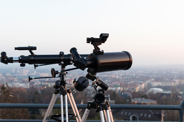 Two professional telescopes, one newtonian and one refractor, mounted on tripods on a rooftop...