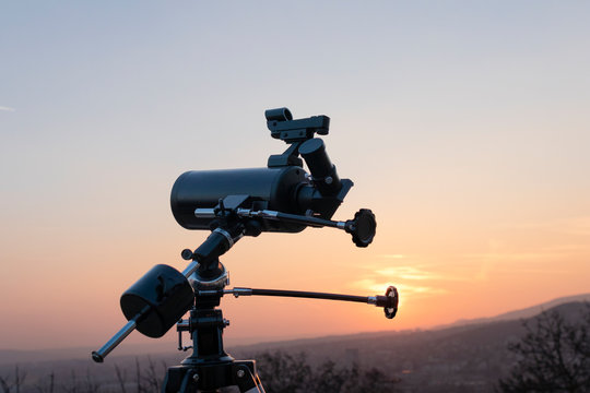 A professional newtonian telescope mounted on a tripod, looking at a major city at sunset