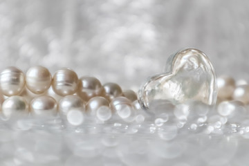 Natural white pearl beads and a transparent heart on a sparkling background