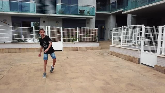 SALOU/SPAIN - MAY 26 2018: Boy trains to play football in tiled courtyard among houses with glass balconies and terraces with white grids  on May 26 in Salou