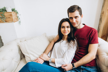 Obraz premium Lovely couple in love in casual clothes sits on the sofa in cozy home, and hugging each other