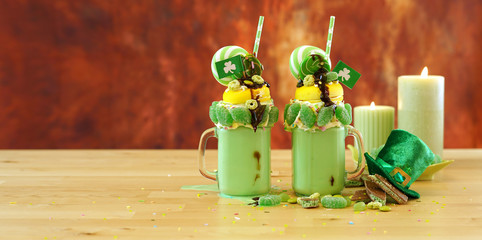 Happy St Patrick's Day on-trend holiday freak shakes milkshakes decorated with candy and lollipops, web size banner with copy space.