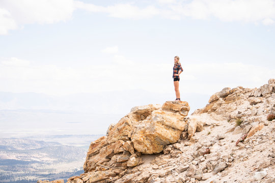 Side view of woman looking at landscape while standing on rocks against cloudy sky