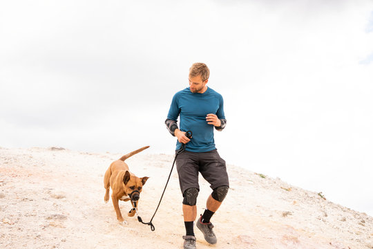 Man with dog walking on mountain against cloudy sky