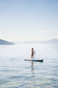 Full length of woman in bikini paddleboarding on lake against blue sky during sunny day