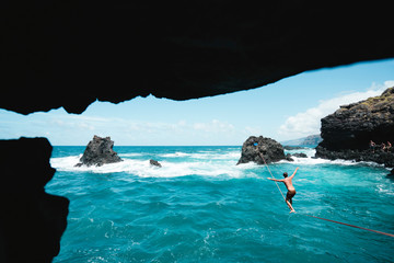 Full length of shirtless young man practicing slacklining over sea
