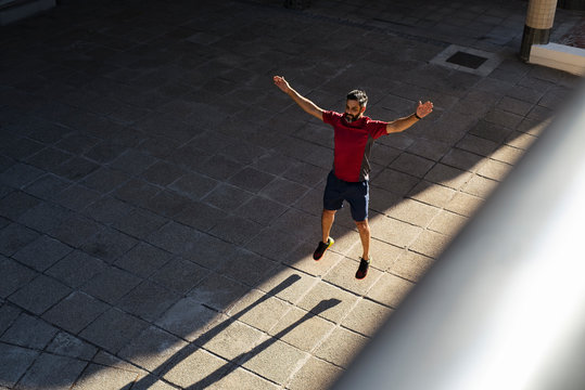 High angle view of confident man with arms raised jumping on footpath in city