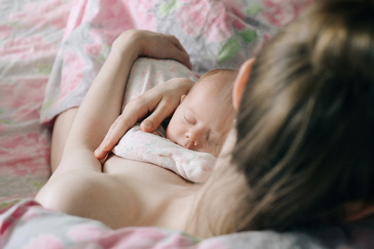 High angle view of topless mother holding cute sleeping daughter while sitting on bed at home