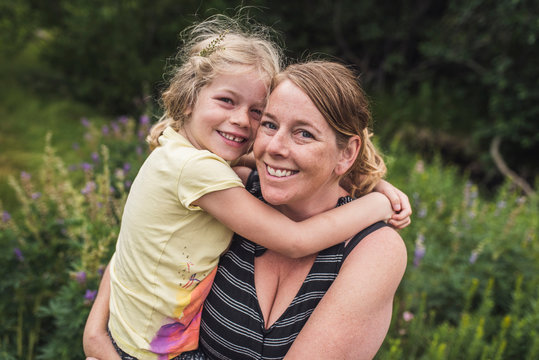 Portrait of happy mother carrying daughter while standing on grassy field in forest