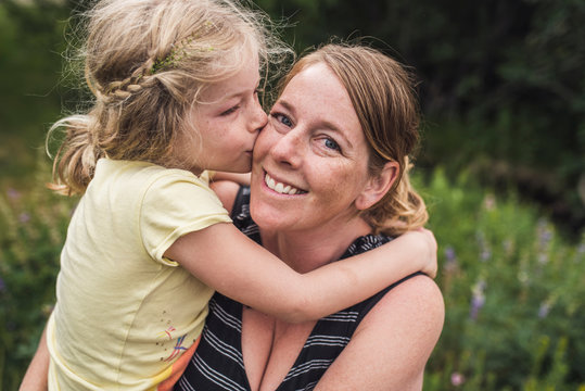 Side view of daughter kissing mother standing on field in forest