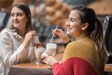 Two happy women are sitting in a cafe, drinking milkshakes,