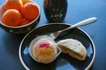 Chinese winter melon and red bean cakes with bowl of mandarin oranges, in black mid-century modern dishware.    